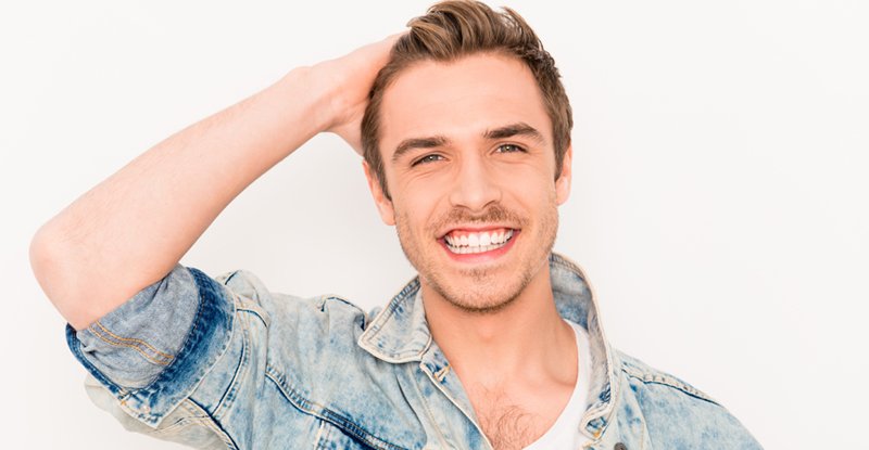 Man smiling with a full head of blonde hair transplant hair wearing denim top